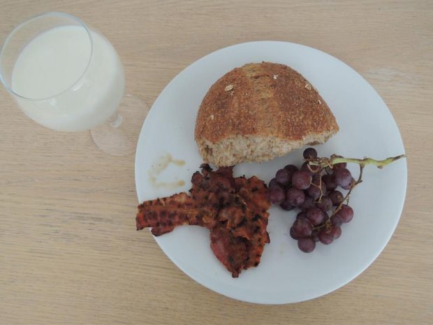 Un trozo de pan, tocino, uvas y leche.